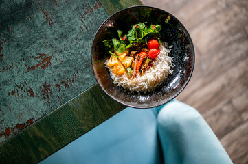 Top view of a colorful rice bowl with vegetables, pineapple, and herbs on a rustic green wooden...