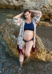 Beautiful pregnant woman posing in a bikini next to the rocks by the sea.
