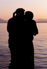 silhouette of a couple kissing in the calm waters of the sea, on the shore of the beach, at sunset