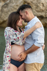 A beautiful couple embracing on the beach, with the man touching his pregnant wife's belly.