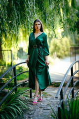 Elegant young woman in a green dress walking confidently on a small arched bridge surrounded by...