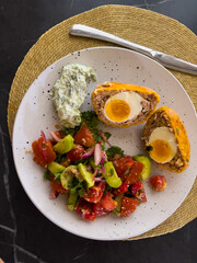 Homemade Scotch eggs served with fresh vegetable salad. Traditional Scottish cuisine prepared at home, a wholesome and healthy meal idea with rich flavor and balanced nutrition.
