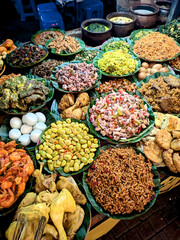 A vibrant, close-up view of a street food stall displaying numerous platters of various traditional Indonesian dishes ready to be chosen by customers.