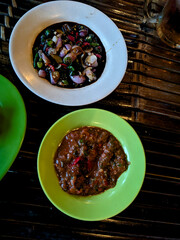  Two vibrant Indonesian sambals, a dark soy sauce-based chili with shallots and a rich red chili paste, displayed in distinct bowls on a traditional bamboo mat, ready to spice up a meal. 