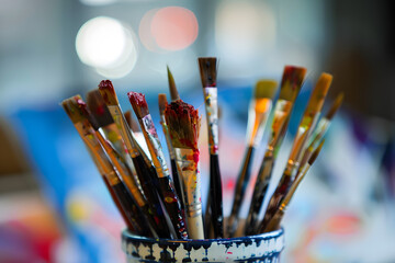 Worn wooden paintbrushes in ceramic jar beside