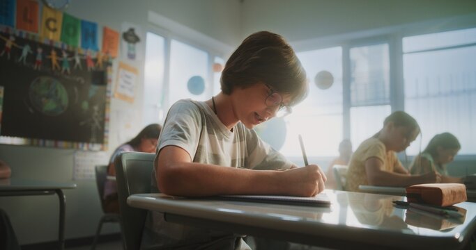 Concentrated Primary School Children Writing School Test on Geography or Ecology in Modern Classroom. Female Teacher Walking Between Desks, Controlling Group of Diverse Kids During the Exam Process.