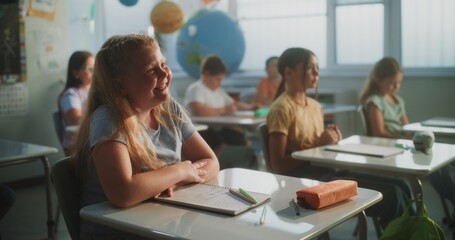 Primary School Children Sitting at the Desks, Listening to Lecture from Teacher, Raising Hands to Give Correct Answer. Group of Young Boys and Girls Learning Geography or Science in Modern Classroom.