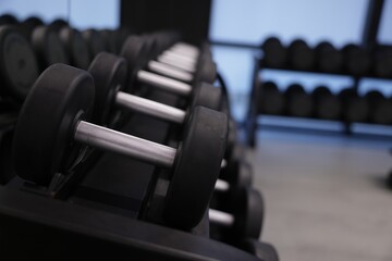 Many metal dumbbells on stand in gym, closeup