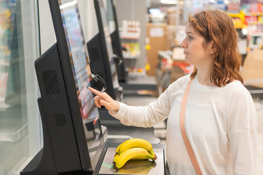 Caucasian woman using self-checkout technology at grocery store. 