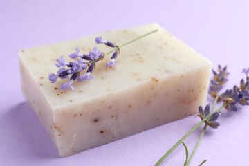 Aromatic soap bar and lavender flowers on violet background, closeup