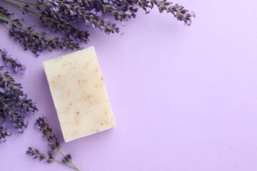 Aromatic soap bar and lavender flowers on violet background, flat lay. Space for text