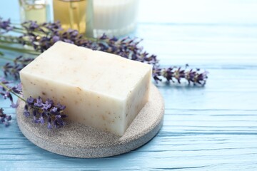 Aromatic soap bar and lavender flowers on light blue wooden table, closeup. Space for text