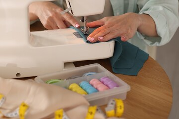 Woman working with sewing machine and fabric at table in workshop, closeup