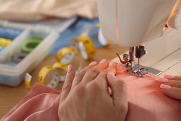 Woman working with sewing machine and fabric in workshop, closeup