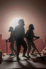 Three silhouetted figures, appearing to be anthropomorphic monkeys in gas masks, stand against a bright, hazy, reddish-orange background, holding tools.