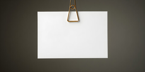 A blank white card gently gripped by a brass alligator clip suspended from a minimal wire frame, soft backlight glow