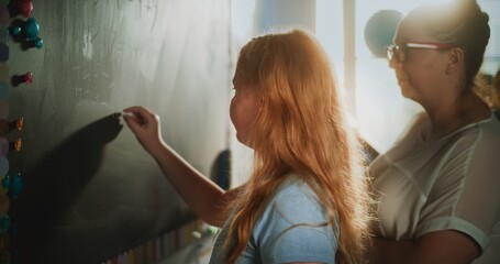 Smart Pupil Showcasing Math Knowledge: Static Shot of Elementary School Girl Solving Mathematical Problems Writing on the Chalkboard in Classroom. Female Teacher Checking Answers, Helping Student.