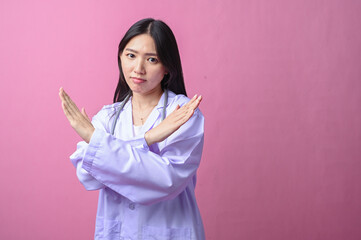 Asian female doctor in a white lab coat making an X sign with her arms, expressing disapproval or...