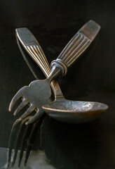 Ancient worn vintage cutlery on the black background. Crossed black metal spoon and fork in dark...
