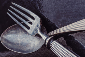 Close-up of Ancient worn vintage cutlery on the dark background. Crossed black metal spoon and fork...