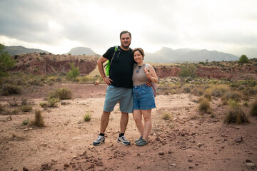 A couple poses together in a rocky desert area, surrounded by rugged terrain and distant mountains....