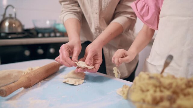 Mom and daughter cooking food. Little girl helps her mother prepare dinner. Family makes dumplings at home in the kitchen.