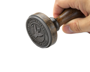 A hand holding a round stamp with an eagle design and text around the edge against black background