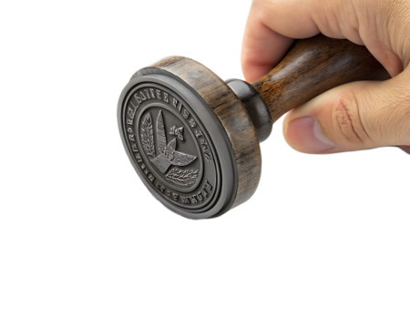 A hand holding a round stamp with an eagle design and text around the edge against black background - Powered by Adobe