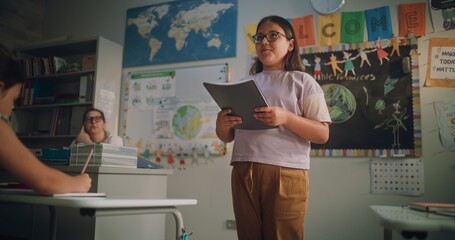 Primary School Girl Holding Notebook Speaking, Showcasing Knowledge of Geography in Front of...