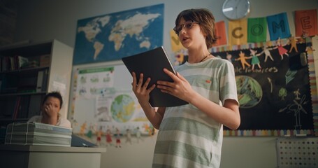 Renewable Energy Lesson: Elementary School Boy Holding Notebook Speaking, Giving Presentation on...