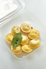 A Tasty Assortment of Yellow Dumplings with a Bay Leaf Garnish in a Clear Plastic Container Perfect for Culinary Exploration and Enjoyment