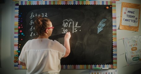 Back View of Female Teacher Writing on the Chalkboard, Explaining Multiplication and Division to...