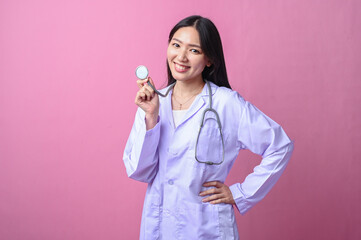 Asian female doctor smiling while holding stethoscope chest piece near her face, wearing white coat...
