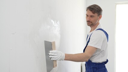 Male construction worker wearing protective gloves and blue construction coveralls, spreading...