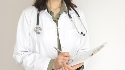 Female doctor, wearing a stethoscope and a medical coat over a green blouse, is standing and...