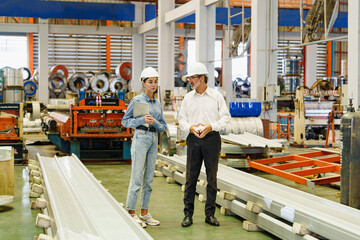 Senior engineer and female staff discussing near metal roofing production line in modern factory,...