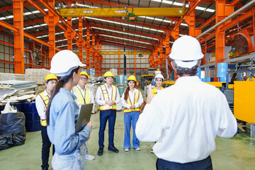 Senior engineer giving team briefing inside metal roofing factory, with workers listening...