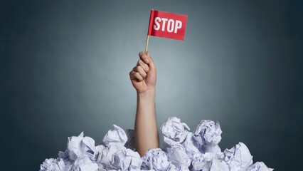 Overwhelmed by work, hand emerges from crumpled paper pile holding STOP sign
