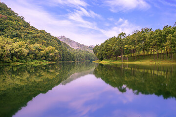 A peaceful lakeside view at Pang Oung, Mae Hong Son, Thailand, showing lush pine forests and crystal-clear reflections in the water.