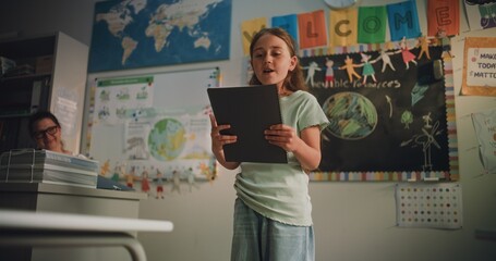 Primary School Girl with Notebook Speaking, Showcasing Knowledge of Ecology in Front of Classmates...