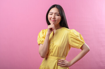 Asian woman in a yellow dress smiling gently with her hand resting under her chin, posing...