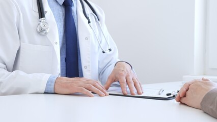 Adult doctor gesturing with hands while explaining diagnosis to patient during medical consultation...