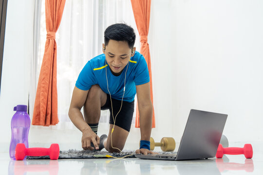 Asian man performing exercise at home with dumbbells and a water bottle nearby. Wellness and Healthy lifestyle concept - Powered by Adobe