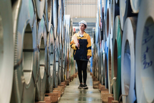 Warehouse scene with metal coils and female inspector recording inventory data. Highlights precision and responsibility in industrial stockkeeping.