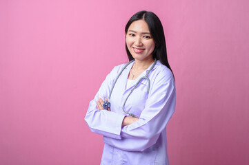 Asian female doctor in white coat and stethoscope smiling confidently with arms crossed, standing...