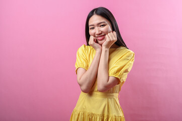 Asian woman wearing a bright yellow dress makes a cute pose with both fists gently resting on her...