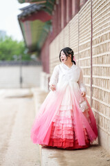 A Korean woman in her twenties wearing a charming pink hanbok walks in front of the traditional...