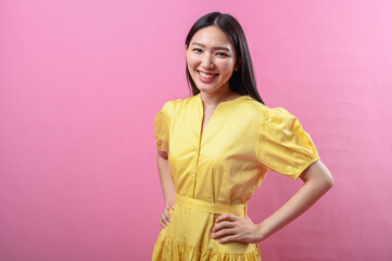 Asian woman with long black hair in a puff-sleeve yellow dress smiling confidently with hands on...