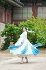 Fototapeta premium A Korean woman in her twenties wearing a sky-blue hanbok twirls gracefully in front of the traditional facade of Gyeongbokgung Palace, her skirt fanning out in elegant ripples, in Seoul in June 2025.