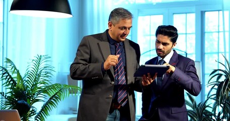 Indian businessmen using tablet computer while standing in modern office, Asian young corporate executives collaborating on digital report, discussing project strategy and data in workplace - Powered by Adobe